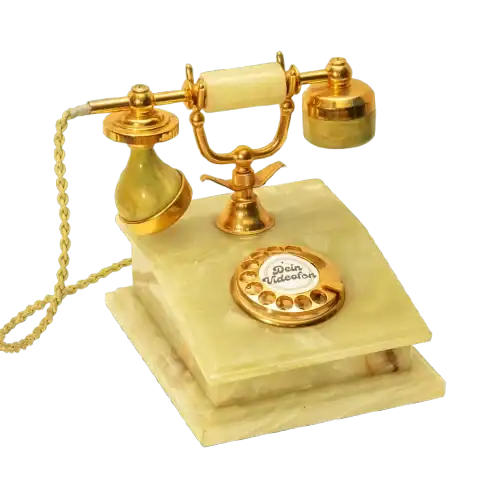 Ein altes Wählscheibentelefon mit goldenen und grünen Akzenten steht auf einem quadratischen Sockel.